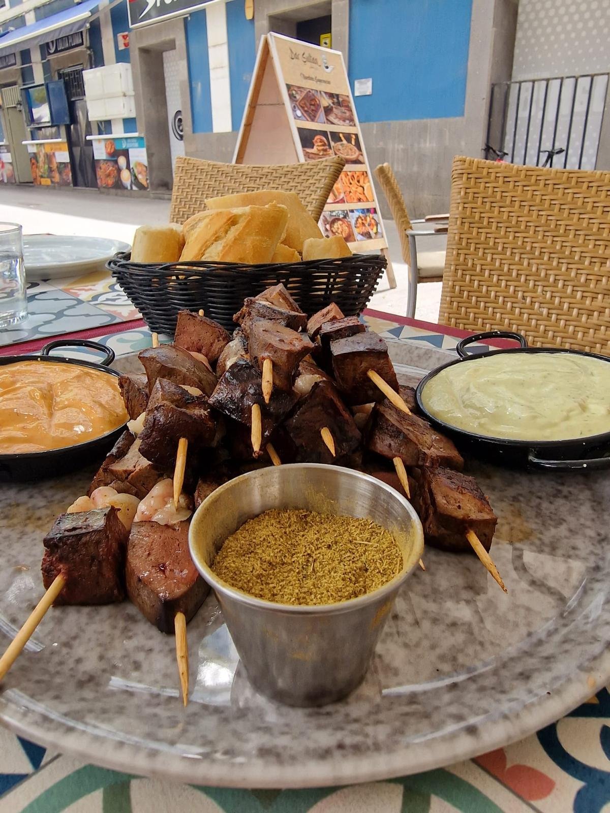 Meat skewers with bread, dips and spices on a terrace table