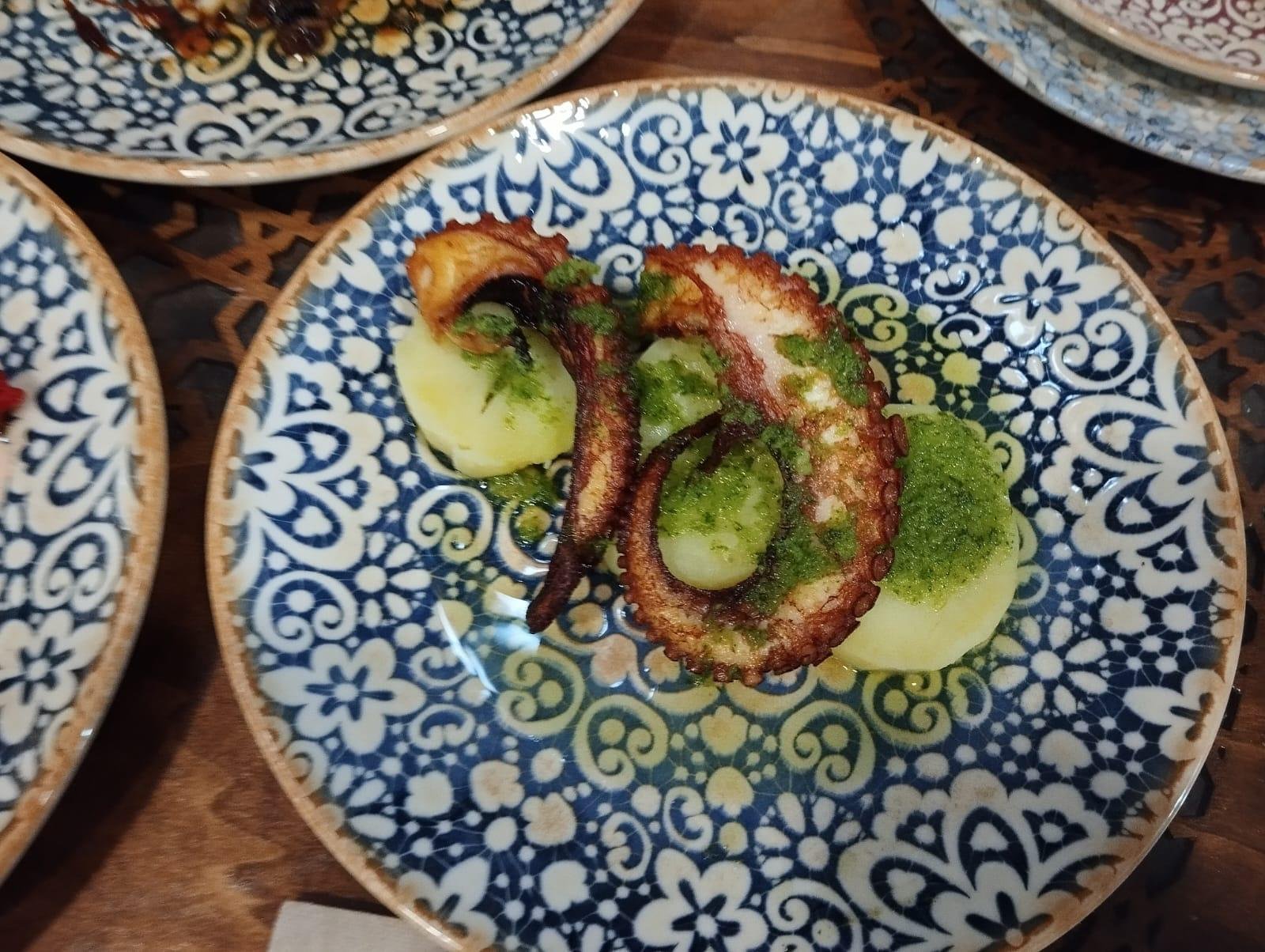 Octopus on potato with green mojo sauce, on a blue patterned plate