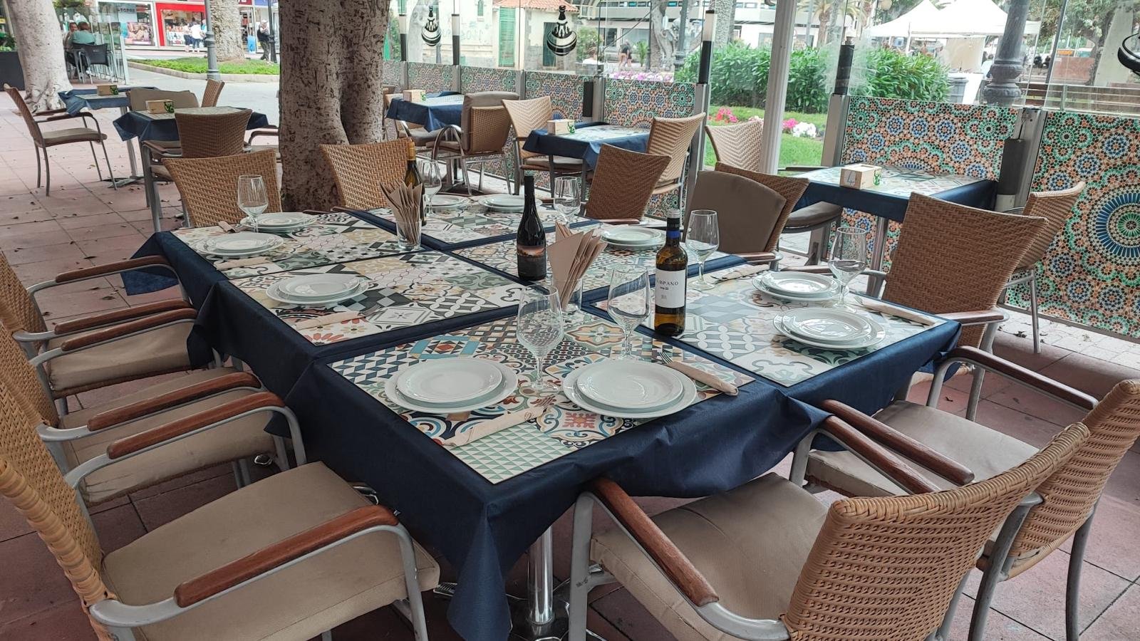 Terrace tables set with navy tablecloths and tiled placemats, with the park gardens behind